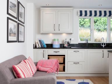 A kitchen with white cabinets black countertop a gray sofa with striped cushions and a pink blanket at Cherrytrees in Rock