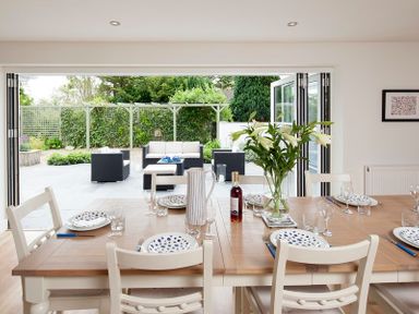 A dining table set with plates glasses and cutlery next to open doors leading to an outdoor patio with seating at Cherrytrees in Rock