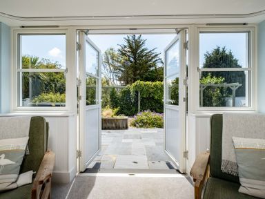A seating area with two armchairs and open doors leading to a garden with stone paving and greenery at Cherrytrees in Rock