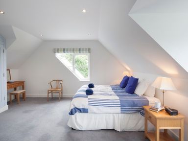 A bedroom with a bed with blue and white bedding a wooden nightstand with a lamp and books a wooden chair and a dressing table with a stool at Cherrytrees Rock