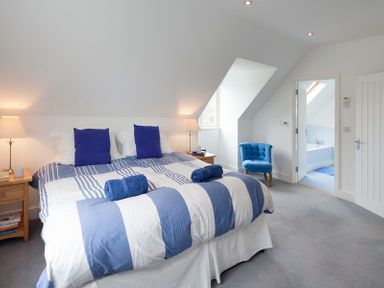 A bedroom with a bed with blue and white bedding two blue pillows two bedside tables two lamps a blue chair and an open door to a bathroom at Cherrytrees in Rock