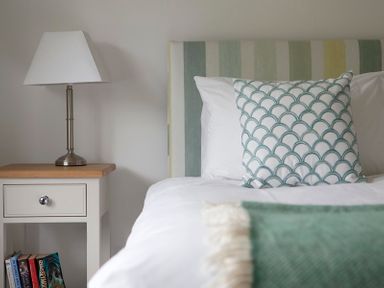 A bedroom with a bed featuring a patterned pillow and a nightstand with a lamp and books at Cherrytrees in Rock