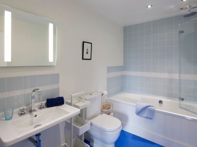 A bathroom with a sink a toilet and a bathtub with blue tiles and a towel at Cherrytrees in Rock