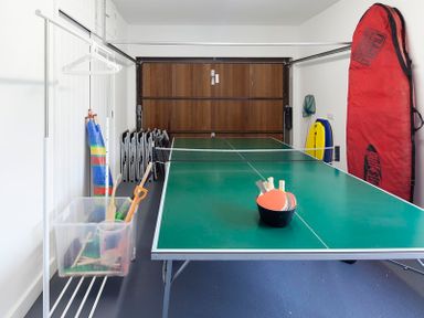 A garage with a ping pong table and paddles a red bag and beach equipment at Cherrytrees in Rock