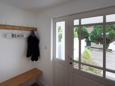 A small entryway with a wooden bench coat hooks and a sign saying beach at Cherrytrees in Rock