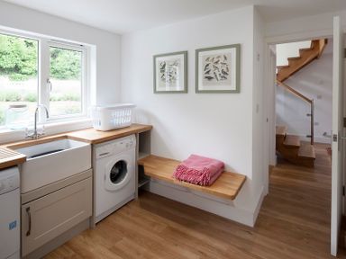 A laundry room with a washing machine sink linens on a bench and framed bird pictures on the wall at Cherrytrees in Rock