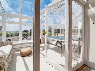 A glass conservatory with wicker chairs and a ping pong table at The Haven in Daymer Bay