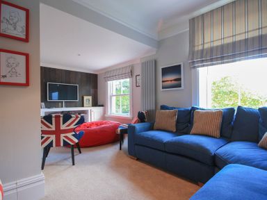 A living room with a blue sofa brown striped cushions union jack chairs a red bean bag a wall mounted tv and window blinds at The Haven in Daymer Bay
