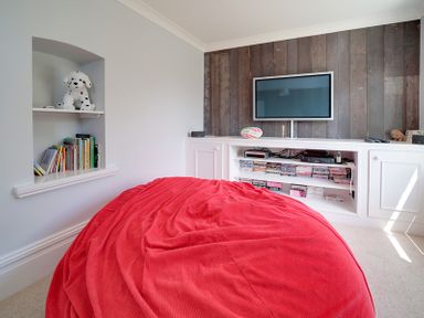 A room with a red bean bag chair facing a wall-mounted TV and shelves with books and DVDs at The Haven in Daymer Bay