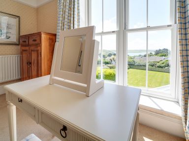 A white dressing table with a mirror in front of large windows showing a garden at The Haven in Daymer Bay