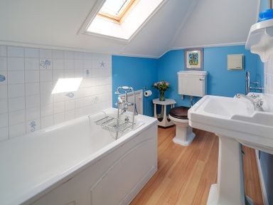 A bathroom with a bathtub toilet sink skylight and small table with flowers at The Haven in Daymer Bay