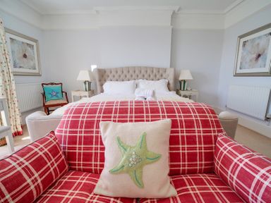A bedroom with a bed bedside tables lamps and a red plaid armchair with a starfish pillow at The Haven in Daymer Bay