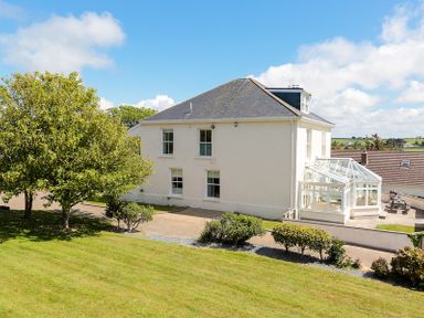 A two-story house with a glass conservatory surrounded by trees and shrubs at The Haven in Daymer Bay