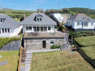 A rear view of a house with a raised patio and garden area at Pendaveli in Polzeath