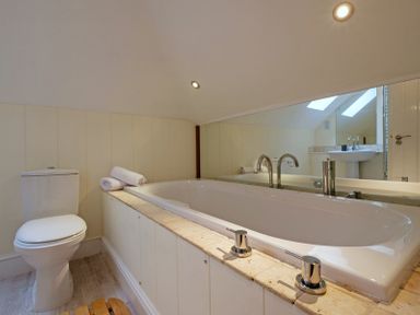 A bathroom with a bathtub and a toilet with towels on the bathtub edge at Pendaveli in Polzeath