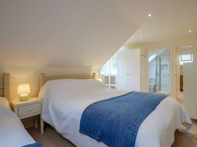 A bedroom with two beds bedside table with lamp white wardrobe and en suite bathroom at Pendaveli in Polzeath