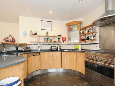 A kitchen with wooden cabinets black countertops stainless steel oven and open shelves at Pendaveli in Polzeath