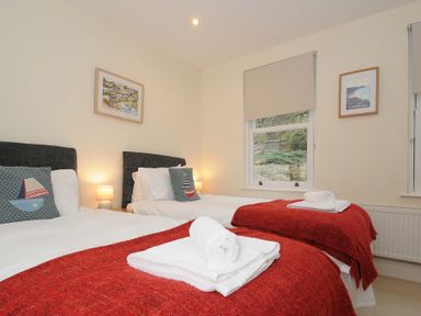 A bedroom with two single beds with red blankets and white towels on top at Pendaveli in Polzeath