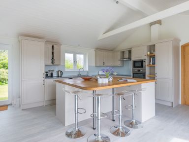 A kitchen with a wooden island countertop and three bar stools at Penny Liggan in Rock
