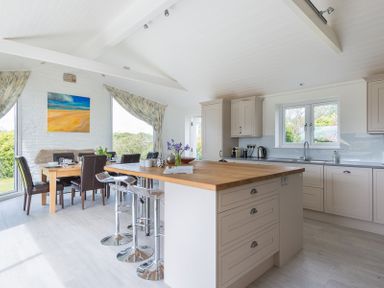 A kitchen with an island and stools next to a dining table with chairs and windows at Penny Liggan in Rock