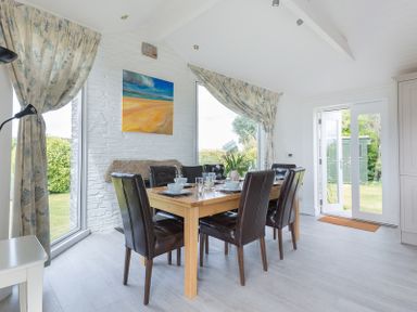 A dining room with a wooden table set for six and leather chairs near large windows and white door at Penny Liggan in Rock