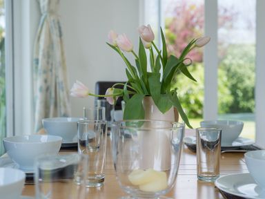 A dining table set with white bowls glasses and a pitcher with pink tulips at Penny Liggan in Rock