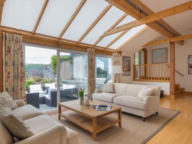 A living room with beige sofas and a wooden coffee table under a glass roof at Penny Liggan in Rock