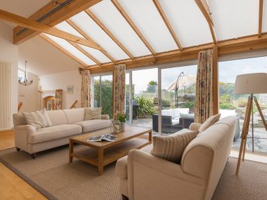 A living room with two beige sofas and a wooden coffee table in front of glass sliding doors at Penny Liggan Rock