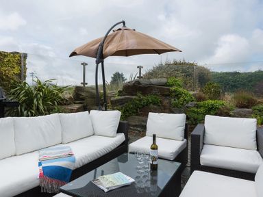 An outdoor seating area with white cushions a glass table an umbrella and plants at Penny Liggan in Rock