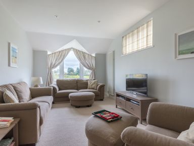 A living room with sofas a round ottoman a coffee table with a game a television and a window with curtains at Penny Liggan Rock