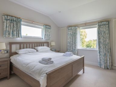 A bedroom with a wooden bed two windows with floral curtains and bedside tables at Penny Liggan in Rock