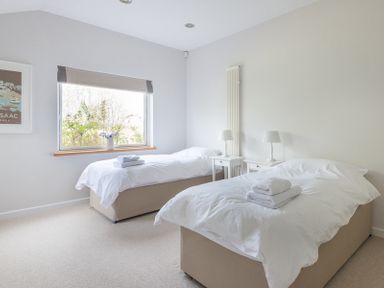 A bedroom with two single beds side by side with white bedding and towels and bedside tables with lamps at Penny Liggan in Rock