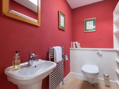 A bathroom with a sink mirror towel rail toilet and artwork on red walls at Penny Liggan Rock