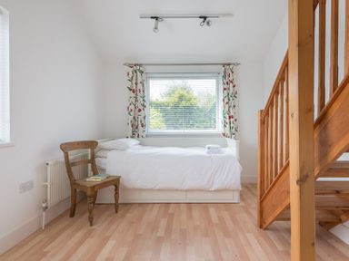 A bedroom with a single bed white bedding wooden chair with books floral curtains and wooden staircase at Penny Liggan Rock