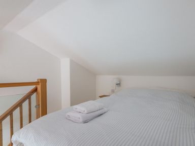 A bedroom with a bed and folded towels next to a wooden staircase railing at Penny Liggan in Rock