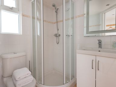 A bathroom with a shower enclosure toilet with towels and a sink with a mirror at Penny Liggan in Rock