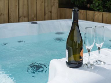 A bottle of champagne and two empty glasses on the edge of a hot tub at Westray House in Polzeath