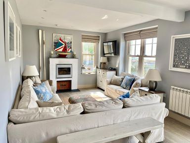 A living room with beige sofas blue cushions a fireplace and a television at Westray House in Polzeath