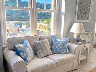 A living room with a white sofa with three cushions next to a side table with a lamp at Westray House in Polzeath