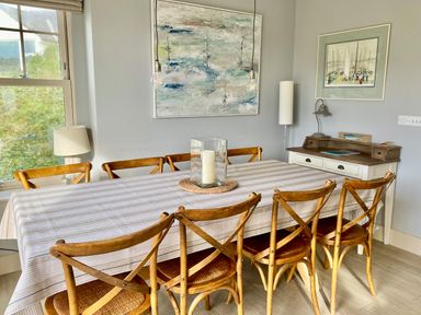 A dining room with a large table covered by a striped tablecloth surrounded by eight wooden chairs at Westray House in Polzeath