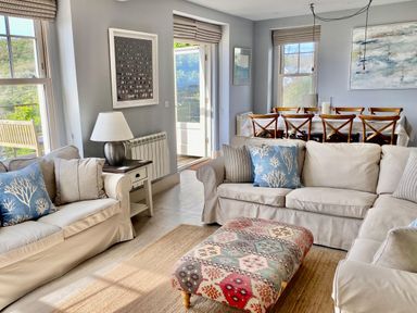 A living room with sofas cushions and a patterned ottoman and a dining table with chairs at Westray House in Polzeath