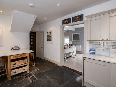 A kitchen with wooden island and stools next to a doorway leading to a living room with a sofa at Westray House in Polzeath