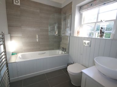 A bathroom with a bathtub and shower next to a window with a toilet and sink at Westray House in Polzeath