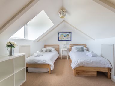 A bedroom with two single beds a nightstand and a window at Westray House in Polzeath