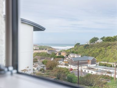 A coastal village with houses and greenery viewed through a window at Westray House in Polzeath