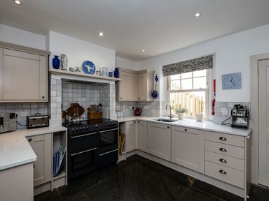 A kitchen with beige cabinets a black stove and oven a window with a floral blind and kitchen appliances at Westray House in Polzeath