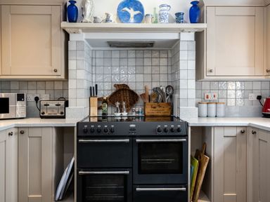 A kitchen with a black double oven stove surrounded by beige cabinets and white tiled walls at Westray House in Polzeath