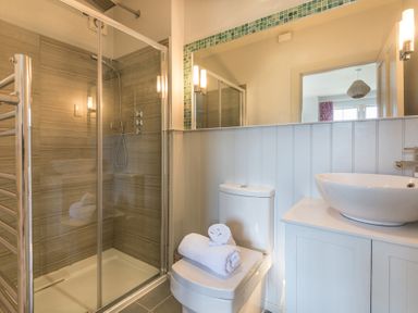 A bathroom with a glass shower enclosure a toilet with towels and a sink on a cabinet at Westray House in Polzeath