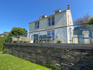 The exterior of a two story white house with a glass railing balcony and outdoor seating at Westray House in Polzeath
