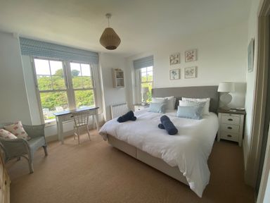 A bedroom with a double bed bedside tables table chair and windows with views at Westray House in Polzeath